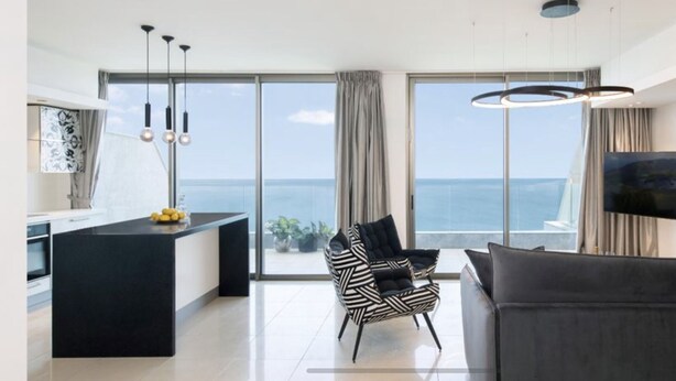 Een moderne woonkamer met een zwarte bank, een zwart-wit gestreepte fauteuil, een keukeneiland en een groot televisiescherm.