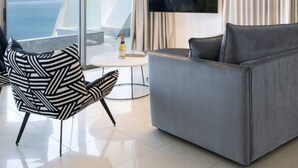 Een moderne woonkamer met een groot raam, een grijze bank, een zwart-witte stoel en een flatscreen televisie.