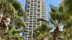 Een hoog gebouw met meerdere balkons, omgeven door palmbomen en een verzorgd gazon.