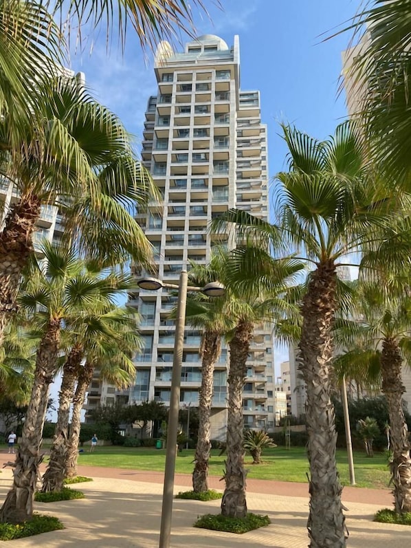 A high-rise building with multiple balconies, surrounded by palm trees and a well-maintained lawn.