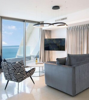 A modern living room with a large window, a grey sofa, a black and white chair, and a flat-screen TV.