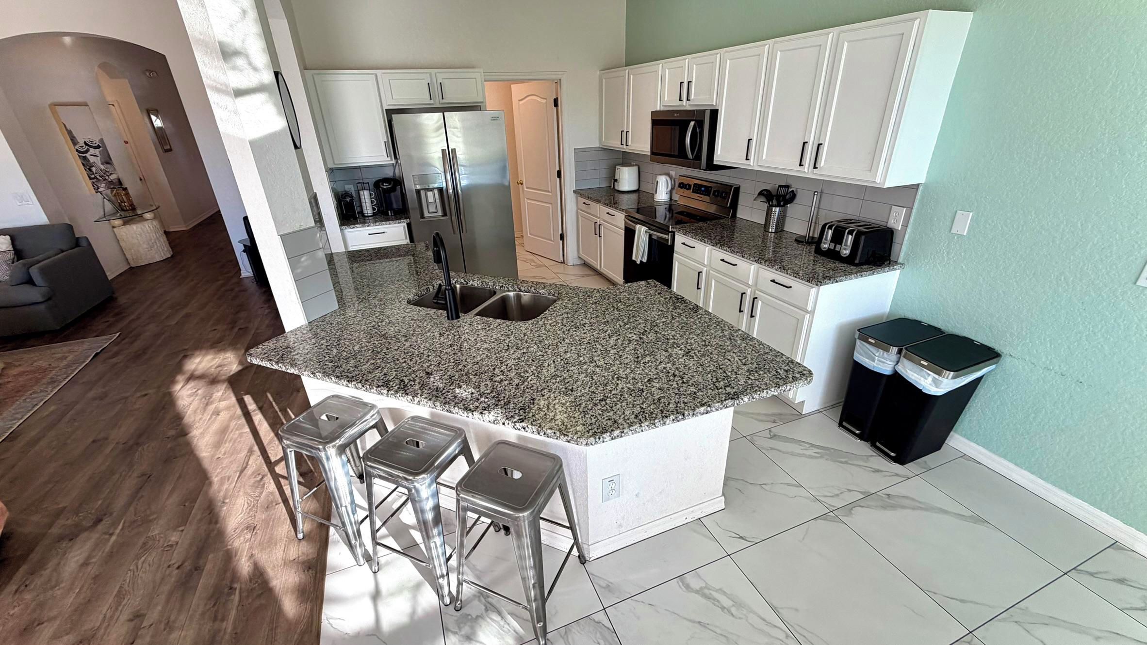 A modern kitchen with granite countertops, stainless steel appliances, and a central island with bar stools.
