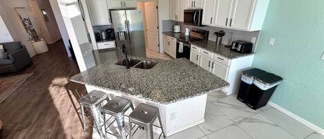 A modern kitchen with granite countertops, stainless steel appliances, and a central island with bar stools.
