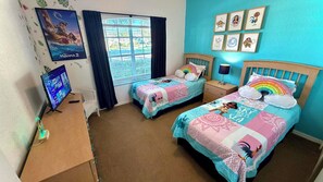 A room with two beds, a TV, a window with curtains, and wall art.