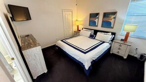 Ein ordentlich eingerichtetes Schlafzimmer mit einem Bett, Nachttischen, einem Fernseher und Kunstwerken an der Wand.