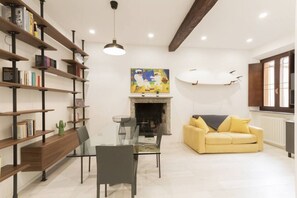 A living room with a fireplace, a yellow sofa, a glass dining table, and bookshelves.