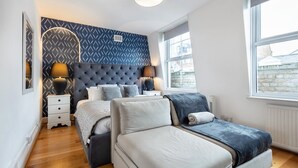 Une chambre à coucher avec un grand lit, une table de chevet, une commode et un mur décoré d’un motif.