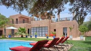 Zona de piscina amb gandules vermelles i un edifici amb grans finestres i balcons.
