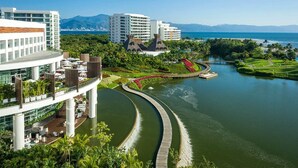 Ein modernes Hotel mit einem gewundenen Wasserkanal, üppiger Vegetation und Blick auf das Meer und die Berge.