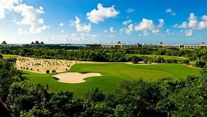 Ein Golfplatz mit einem großen Bunkersand, umgeben von dichter Vegetation und blauem Himmel.