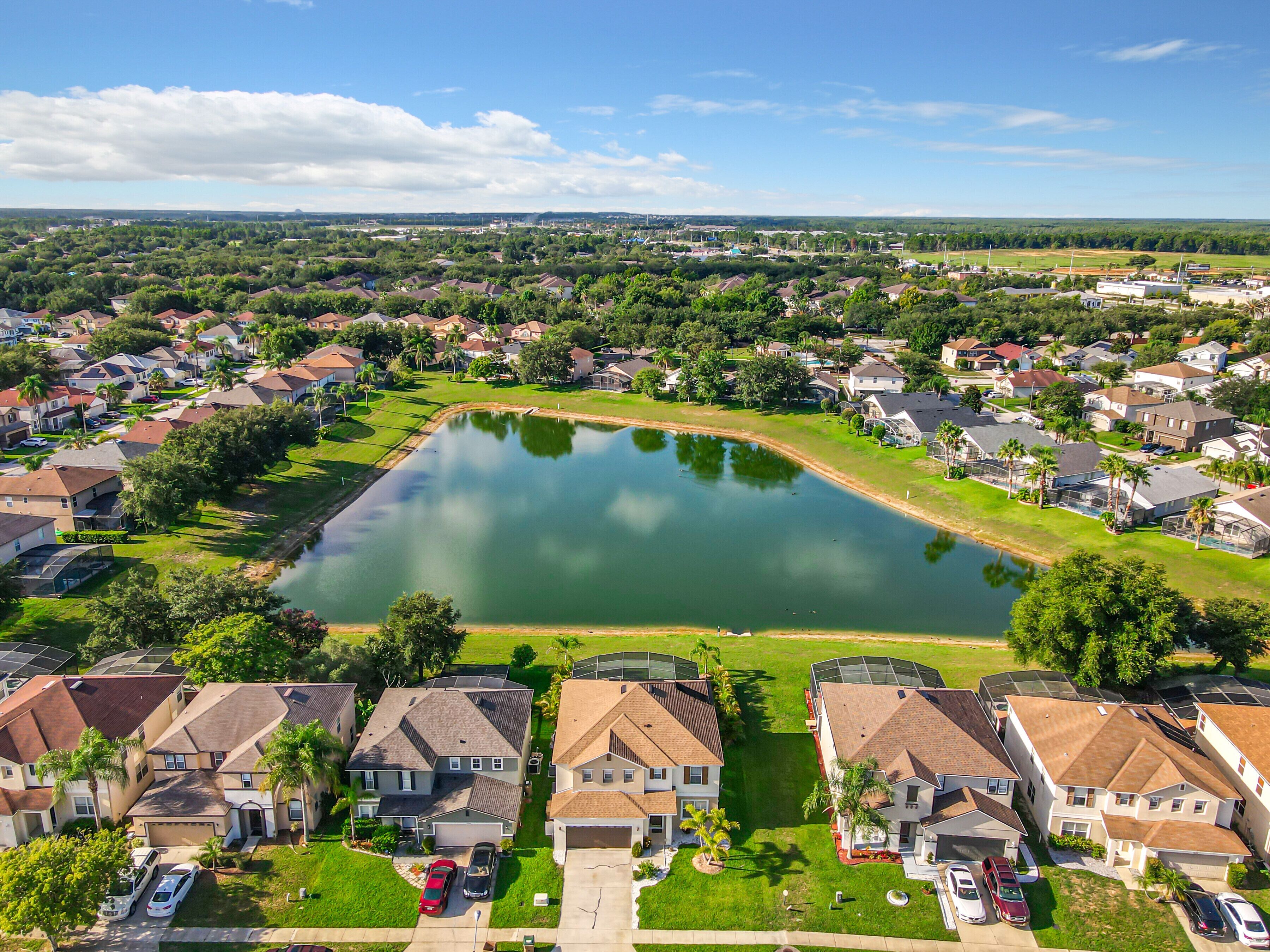 A residential area with houses, a central pond, and a clear sky.