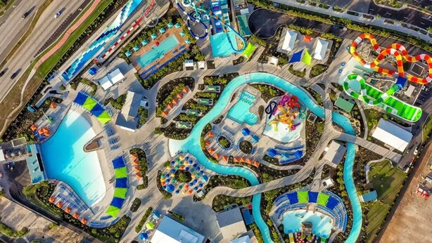 Une vue aérienne d’un parc aquatique avec de nombreux toboggans et piscines, entouré de routes et d’aires de stationnement.