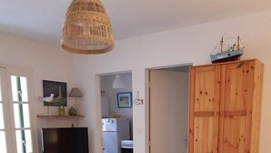 Zona de menjador amb taula rodona de fusta, cadires, lluminària penjant i un armari de fusta amb una maqueta de vaixell a sobre.