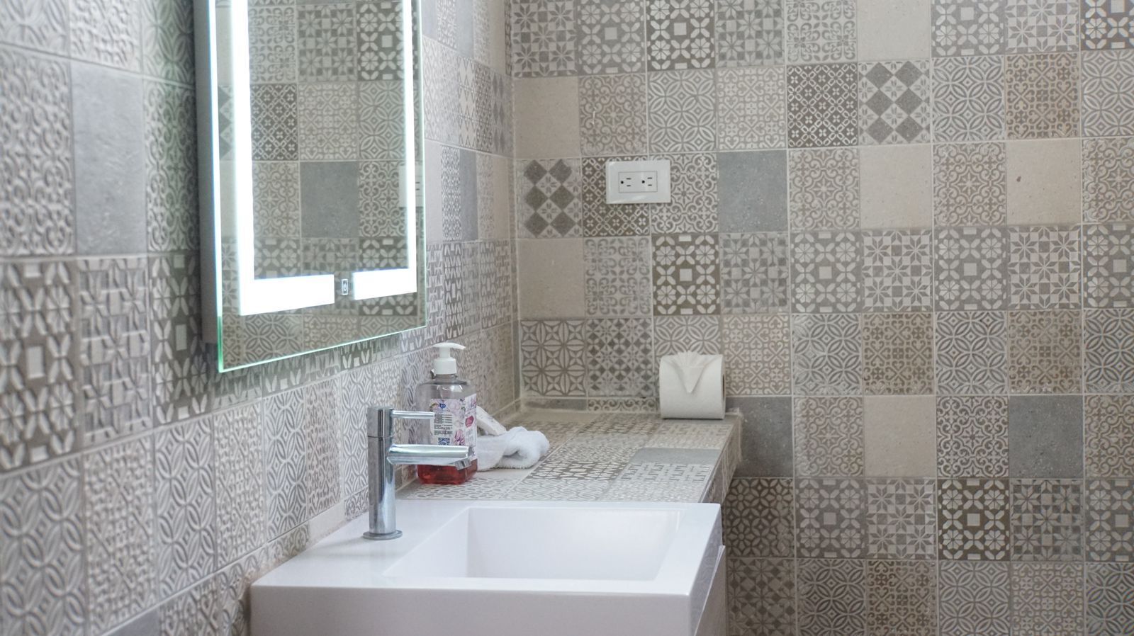 Une salle de bain avec un lavabo blanc, un miroir et des carreaux à motifs.