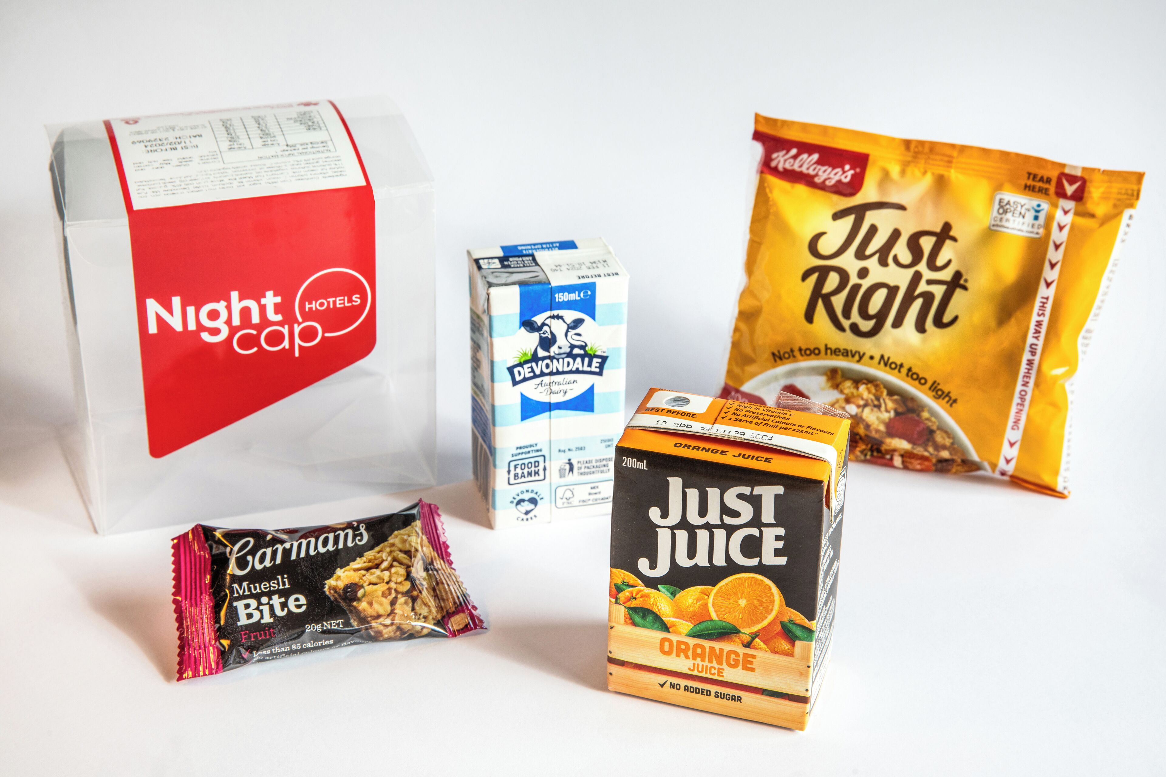 A variety of food items including a carton of Devondale milk, a bag of Kellogg's Just Right snacks, a box of Just Juice orange juice, and a package of Carman's Muesli Bite.