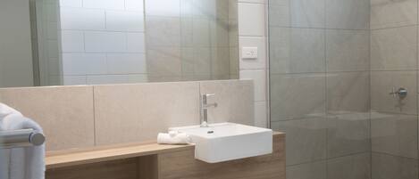 A modern bathroom with a white sink, wooden vanity, and a glass shower enclosure.
