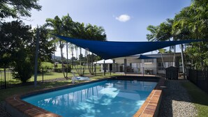 A rectangular swimming pool with a brick edge, surrounded by a gravel area and a grassy lawn. - Apartments at Mission Beach (Mission Beach)