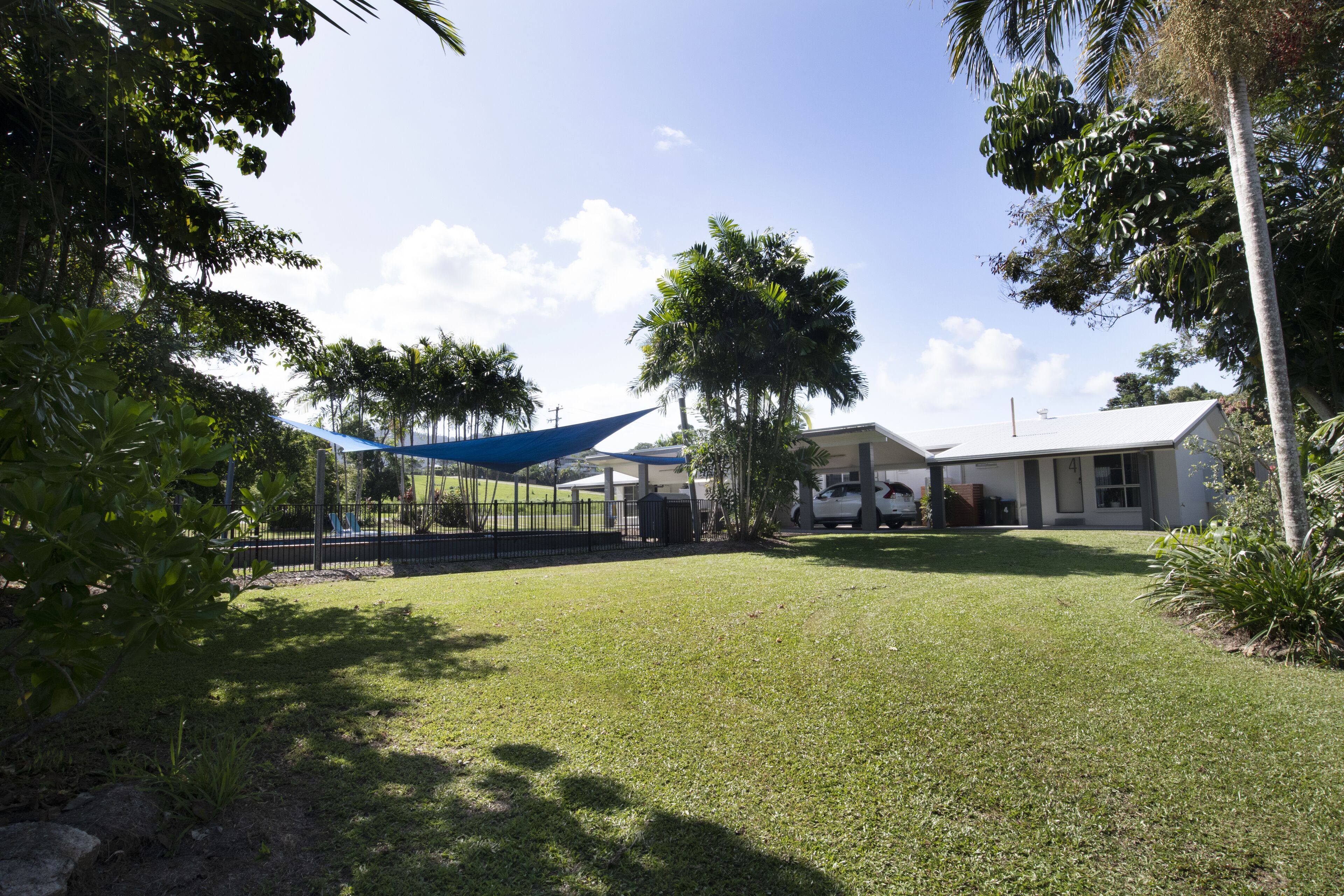 A grassy yard with a blue canopy, a white building, and palm trees.