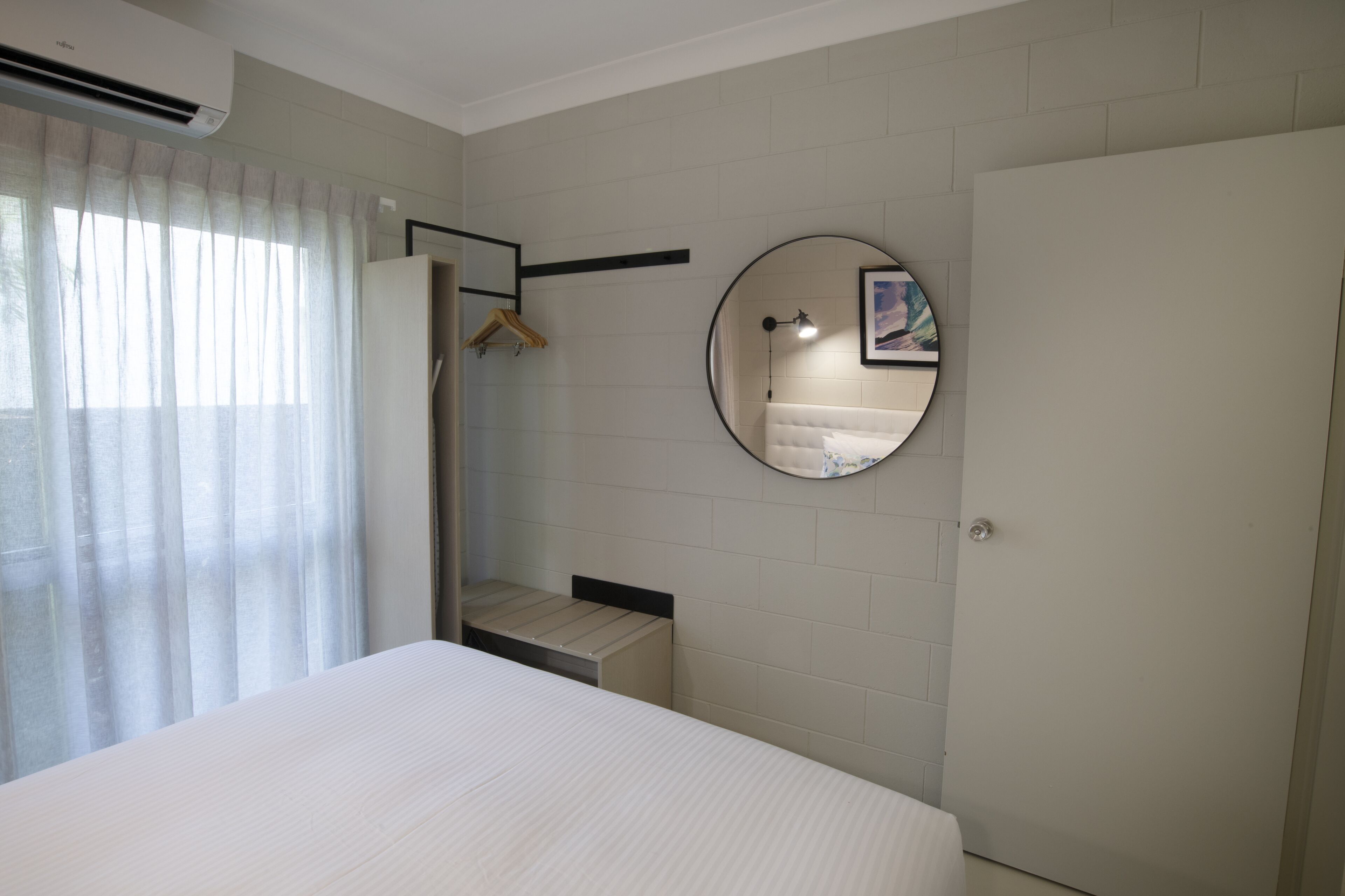 Un dormitorio con cama, un espejo redondo, un armario y una ventana con cortinas.