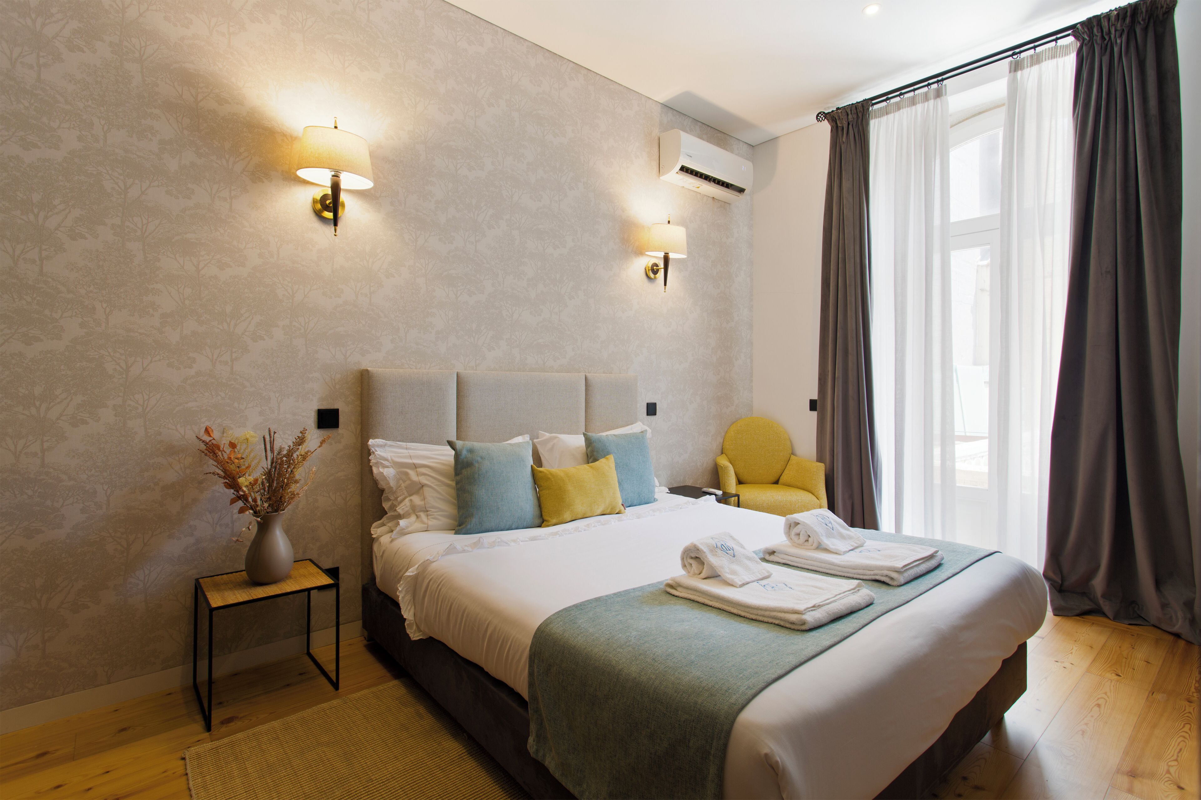 A neatly made bed with pillows, a bedside table with a vase, and a chair.