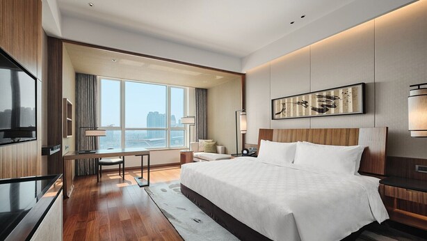 Een moderne hotelkamer met een groot bed, een bureau, een televisie en uitzicht op de stad.