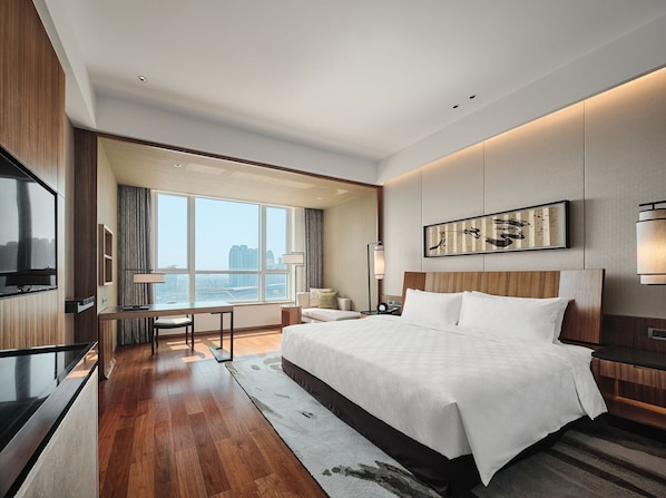 Ein modernes Hotelzimmer mit einem großen Bett, einem Schreibtisch, einem Fernseher und Blick auf die Stadt.
