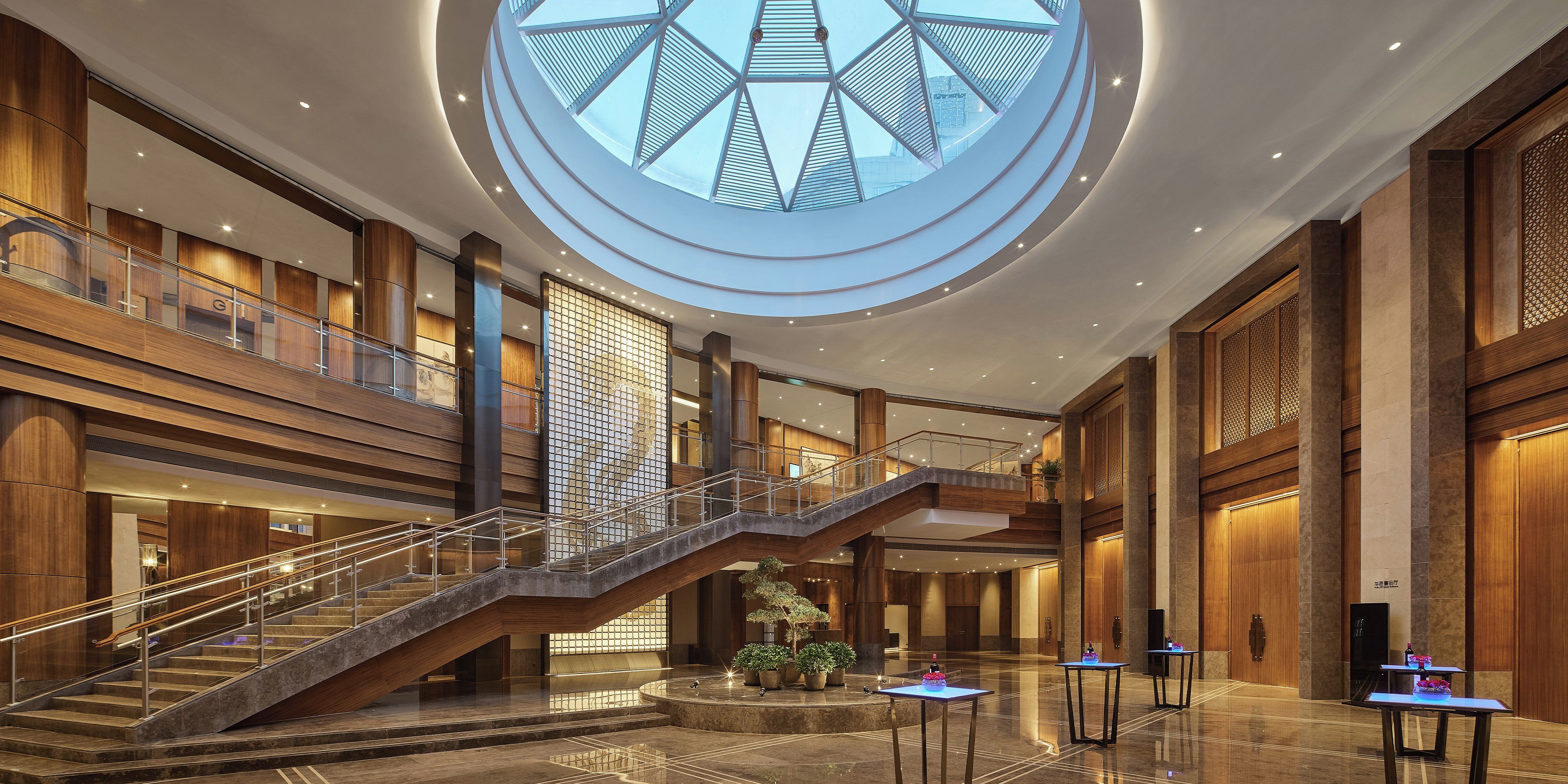 Eine geräumige Hotelhalle mit einer zentralen Treppe, mehreren Ebenen und einem großen Oberlicht.