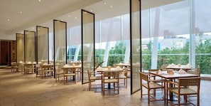 Un restaurant doté d’un sol carrelé à motifs hexagonaux, de meubles en bois et de grandes fenêtres offrant une vue sur la verdure et les bâtiments.