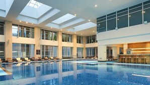 A large indoor swimming pool with multiple lounge areas and a high ceiling with skylights. - Hualuxe Ningbo Harbor City (Ningbo)