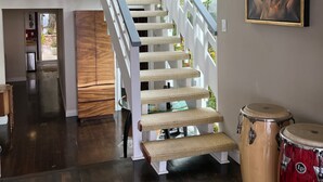 Un escalier avec une rampe blanche et des marches de couleur beige, menant à une pièce d’où l’on peut admirer la verdure environnante.