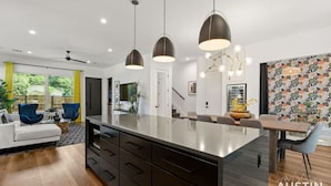A modern kitchen with a central island, pendant lighting, and a dining area with a patterned wall.