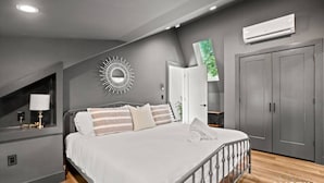 A modern bedroom with a bed, a nightstand, a mirror, and an air conditioning unit.