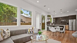 A modern living room with a grey sofa, a glass coffee table, and a dining area with white chairs. There is a kitchen with dark cabinets and stainless steel appliances. - Holly #B xxxxxxxxxxx (Austin)