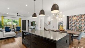 Una cocina moderna con una isla central, iluminación colgante y un comedor con pared decorada.