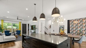 A modern kitchen with a central island, pendant lighting, and a dining area with a patterned wall. - Brand New Luxurious Property + Huge Outdoor Space! (Austin)