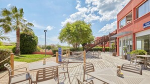 An outdoor patio area with tables and chairs, a palm tree, and a building with a reception sign.