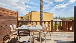 An outdoor patio area with a wooden deck, a white table with chairs, and a palm tree. - Appartement Abordable avec Wi-Fi + Kitchenette (Agde)
