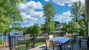 Eine Holzterrasse mit Gartenmöbeln mit Blick auf einen See und ein Haus im Hintergrund.