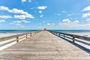 Eine Holzstege, der zu einem Strand führt, mit einem Rettungsturm am Ende.
