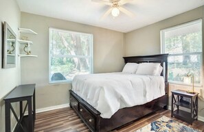 Cozy retreat with a dark bed frame, white bedding, and a small table with a lamp.