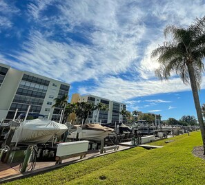 A marina with boats docked, a grassy area, and modern buildings in the background. - Updated unit with canal views,5-minute walk to Gulf beach! (Fort Myers Beach)