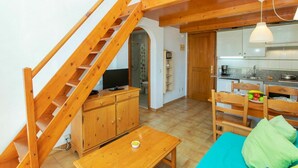 A compact living space with a wooden staircase, a kitchenette, a dining area, and a small bathroom.