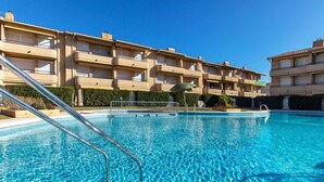 A clear swimming pool with metal ladders, surrounded by a multi-story building with balconies.