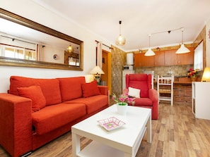 A modern living room with a red sofa, a white coffee table, and a kitchen in the background.