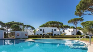 En swimmingpool med en livboj och en skylt, omgiven av vita byggnader och träd.