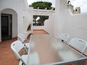 A patio with a glass-top table and white chairs, surrounded by white walls and a tiled floor.