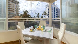 Un coin repas avec une table dressée pour deux personnes, une vue sur le paysage urbain et un balcon agrémenté de palmiers.