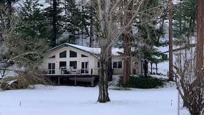 A two-story house with a covered deck, surrounded by snow and trees.