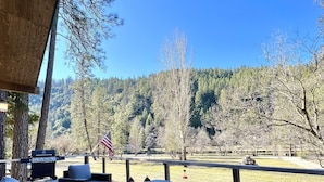 An outdoor deck with seating and a grill, overlooking a forested area.