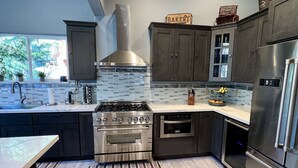 A modern kitchen with dark cabinets, a stainless steel stove, and a large window.